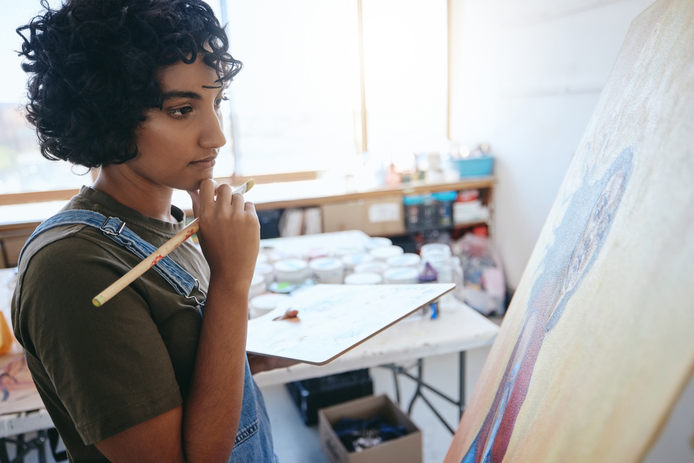 Jonge kunstenaar werkt geconcentreerd aan een schilderij in een licht atelier